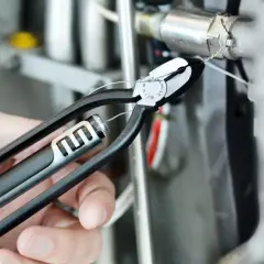 Eine Hand benutzt eine Drahtwirbelzange, um einen Draht an einer technischen Vorrichtung zu sichern.