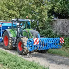 Grüner Traktor mit Anbaugerät und Warnstreifen, erinnert an eine mobile Parkwarntafel, fährt auf Feldweg.