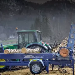 Ein Taifun Holzspalter mit Traktor im Hintergrund, bereit, einen großen Holzstapel zu verarbeiten.