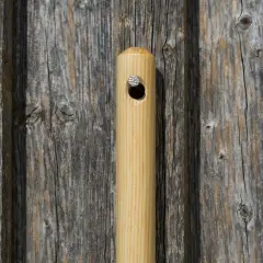 Ein hölzerner Griff, vielleicht von einem Federrechen, mit einem Nagel, der durch ein Loch gesteckt ist, lehnt an einer alten Holzvertäfelung.