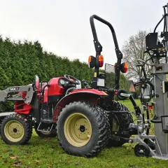 Roter Traktor mit Frontlader und einem liegenden Holzspalter gebraucht 30t im Garten.