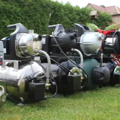 Reihe von Gartenpumpen und Hauswasserwerken auf einer grünen Wiese, bereit für den Einsatz im Garten.