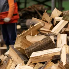 Ein Mann bedient einen roten Holtzspalter, während ein großer Haufen gespaltenes Holz daneben liegt.
