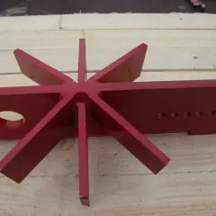 Rotes, sternförmiges Werkzeug mit acht Zacken, das wie ein spaltkreuz universal aussieht, liegt auf Holzbrettern.
