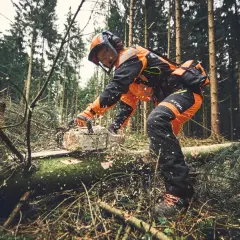 Forstarbeiter in Schutzkleidung arbeitet mit einer Kettensäge im Wald. PSA Forst schützt bei der Arbeit.