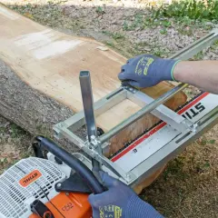Mit einer Kettensäge und einer Führung wird ein großer Baumstamm geschnitten.