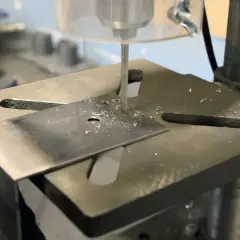 Detailaufnahme des Aufbaus einer Standbohrmaschine, die ein Metallstück bohrt.