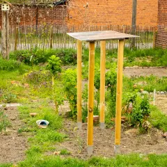 Ein provisorisches tomatendach selber bauen: Holzpfosten mit Metallfüßen tragen eine einfache Dachkonstruktion im Garten.