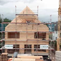 Holzbau im Wohngebiet: Ein Haus aus Holz wird mit Gerüsten und Kran errichtet.