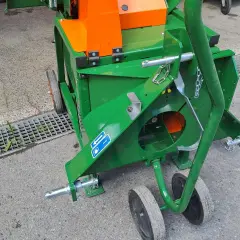 Grüne Wippsäge mit orangefarbenem Gehäuse, bereit für den Einsatz. Die Zapfwelle ist angeschlossen, um Holz zu zerkleinern.