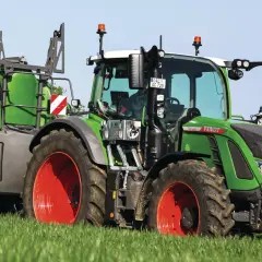 Grüner Fendt-Traktor mit Anhänger auf einem Feld. Die universellen Kabinen für Traktoren bieten Komfort und Sicherheit.
