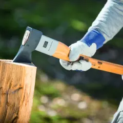 Person mit Handschuhen hält Axt über Holzscheit, bereit, um zu zeigen, wie spaltet man holz.