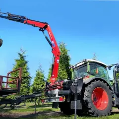 Ein roter Ladekran, gebraucht für Traktor, hebt einen Baum mit Wurzelballen. Der Traktor steht daneben, bereit für den Transport.
