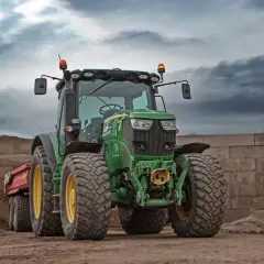 Grüner Traktor mit Anhänger, zwei orangefarbene Rundumkennleuchten auf dem Dach, bereit für den Einsatz auf der Baustelle.