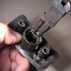 Mit einer Seegeringzange wird ein Sicherungsring aus einem schwarzen Bauteil entfernt.