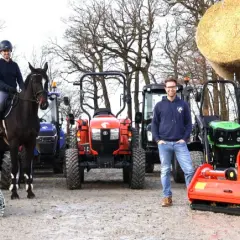 Ein Mann und eine Frau mit einem Pferd stehen vor mehreren Traktoren. Ein kleiner forsttraktor ist im Vordergrund zu sehen.