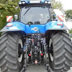 Blauer Traktor mit großen Reifen. An der Seite sind rot-weiße Warnschilder mit Beleuchtung angebracht.