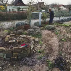 Gartenarbeit im Frühling: Eine Frau steht neben einem Hochbeet, das mit Steinen gemauert ist. Was ist ein Mulcher? Er hilft, den Boden zu bedecken.