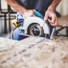 Ein Handwerker sägt mit einer **Baukreissäge** Holz. Sägespäne fliegen durch die Luft.