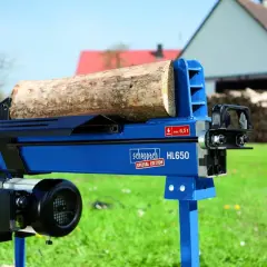 Ein liegender bgu Holzspalter HL650 von Scheppach mit einem Holzstamm bereit zum Spalten. Im Hintergrund ein Haus und Holzstapel.