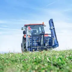 Traktor mit Tajfun RCA 480 auf einem grünen Feld unter blauem Himmel.