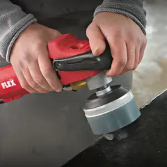 Präzises Stein schleifen mit einem roten Winkelschleifer von Flex. Staub wirbelt auf, während die Kante bearbeitet wird.