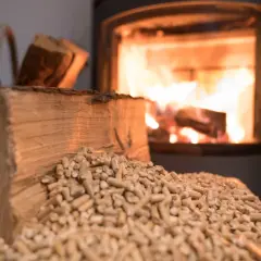 Holzscheite und Pellets liegen bereit, während im Kamin das Feuer lodert. Bauholz im Kamin verbrennen sorgt für wohlige Wärme.