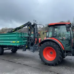 Ein roter Traktor mit einem grünen Anhänger und Ladekran steht bereit für den Einsatz.