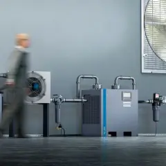 Industrielle Anlage mit Kompressor, Trockner und Luftbehälter. Ein Mitarbeiter mit Hubwagen im Vordergrund. Regelmäßiges kompressor wasser ablassen ist wichtig für die Effizienz.
