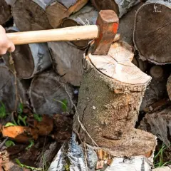 Mann spaltet Holz mit Axt. Der Stapel zeigt, wie man Holz stapeln kann, mit Rinde nach oben oder unten.