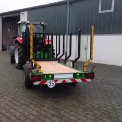 Ein roter Traktor mit einem neuen meterholzwagen mit kran steht vor einer Halle.