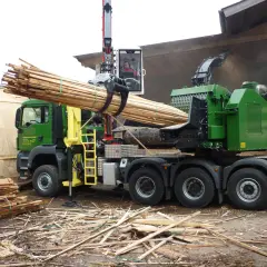 Grüner Holzhacker LKW mit Kran lädt Holzstämme. Der Hacker zerkleinert Holz zu Hackschnitzeln.