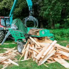 Ein Traktor mit einem Holzspalter, der gerade einen Baumstamm zerteilt. Ein gebrauchter Schichtholzspalter im Einsatz.