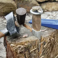 Werkzeuge zum Birken spalten: Beil, Spalthammer und Keil liegen bereit. Ein Holzstamm ist bereits angespalten.