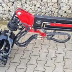 Detailaufnahme eines roten und schwarzen Schwenkwerks für Forstkran mit Greifer und Hydraulikschläuchen.