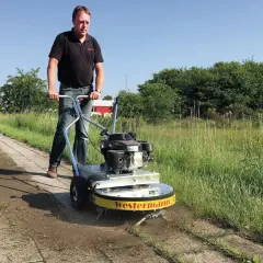 Mann mit Westermann Wildkrautbürste auf einem Gehweg, um Unkraut zu entfernen.