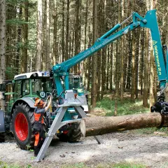 Ein Mann bedient den Kran eines Traktors im Wald. Das Schwenkwerk des Krans greift einen Baumstamm.