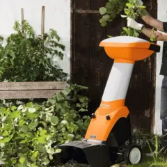 Ein Mann mit Schutzbrille und Gehörschutz bedient einen orange-weißen Holzhacker. Die Zapfwelle des Geräts ist bereit für den Einsatz im Garten.