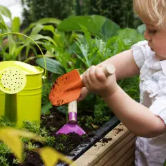 Kleines Kind mit Schaufel im Garten, lernt, wie man ein kinder hochbeet selber baut. Grüne Gießkanne daneben.