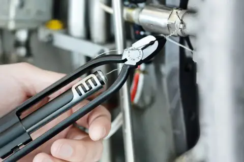 Eine Hand benutzt eine Drahtwirbelzange, um einen Draht an einer technischen Vorrichtung zu sichern.