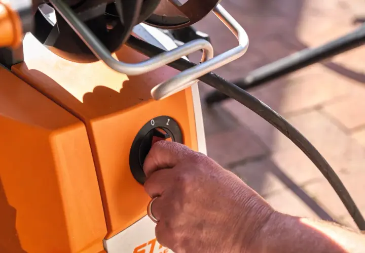 Hand dreht Schalter am orangefarbenen Hochdruckreiniger, bereit, ihn an den Wasserhahn anzuschließen.
