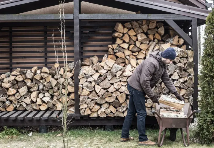 Mann mit blauer Mütze lagert anmachholz in einer Schubkarre. Der Holzstapel hinter ihm ist beeindruckend.