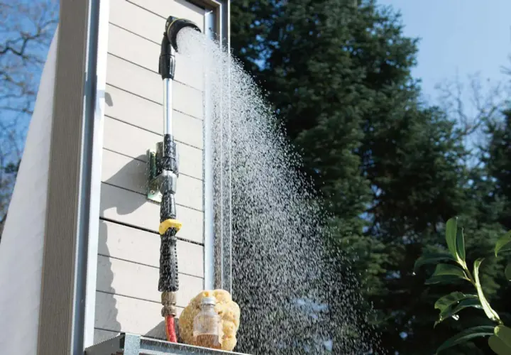 Eine Gartendusche, die man selber bauen kann, sprüht erfrischendes Wasser. Ein Schwamm und eine kleine Flasche stehen bereit.