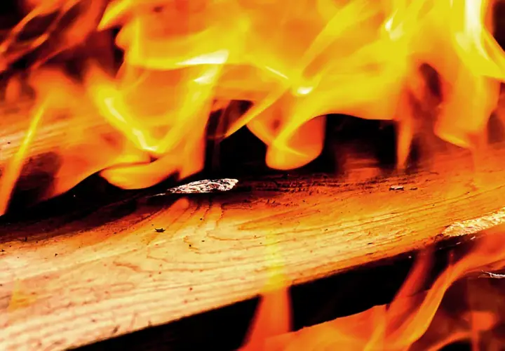 Flammen tanzen über Holz. Lackiertes Holz verbrennen giftig, hinterlässt Asche und Rauch.