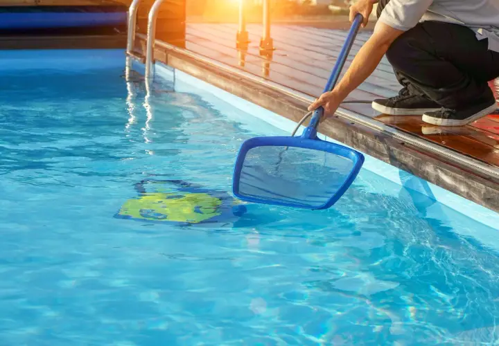 Mann reinigt den Pool mit einem Kescher. Ein gelbes Spielzeug schwimmt im klaren Wasser.
