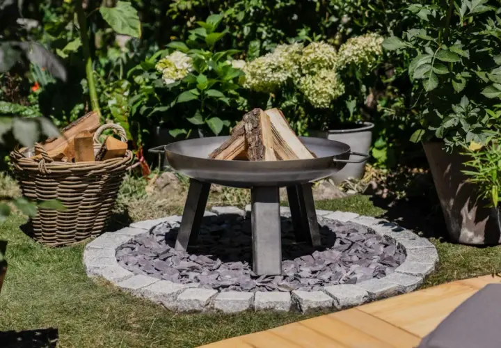 Schöne Feuerstelle im Garten mit Holzkorb und Pflanzen. Tolle Feuerstelle Garten Ideen für gemütliche Abende.