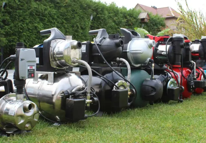 Reihe von Gartenpumpen und Hauswasserwerken auf einer grünen Wiese, bereit für den Einsatz im Garten.