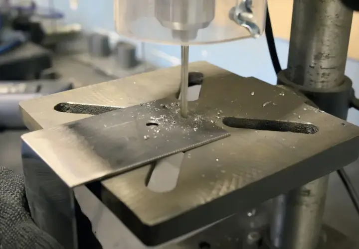 Detailaufnahme des Aufbaus einer Standbohrmaschine, die ein Metallstück bohrt.