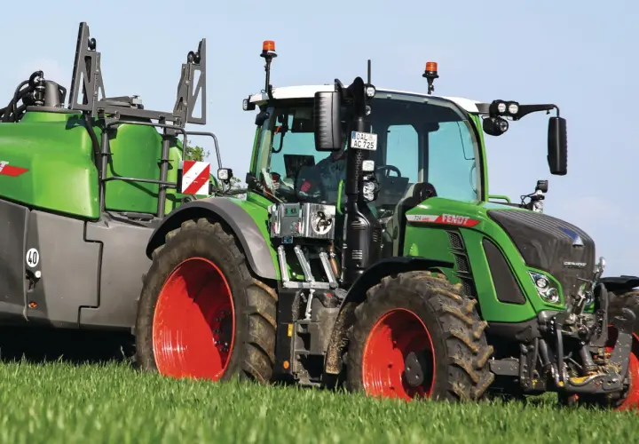 Grüner Fendt-Traktor mit Anhänger auf einem Feld. Die universellen Kabinen für Traktoren bieten Komfort und Sicherheit.