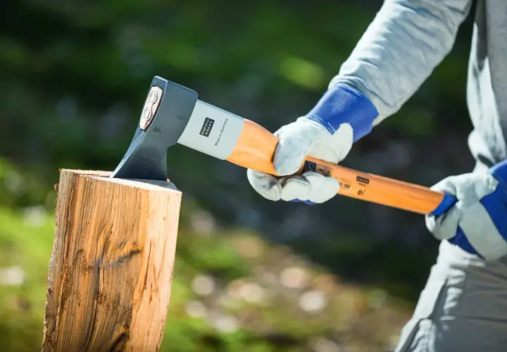 Person mit Handschuhen hält Axt über Holzscheit, bereit, um zu zeigen, wie spaltet man holz.